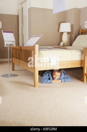 Junge versteckt unter Bett im Möbelhaus Stockfoto