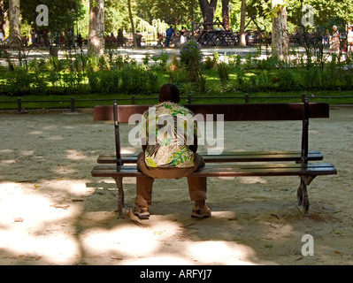 Ein junger afrikanischen Mann sitzt ruhig auf einer Bank in einem Park in Montpellier, Südfrankreich Stockfoto