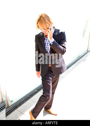 Ein junger kaukasischer Geschäftsmann auf seinem Handy checkt seine eigenen Schuhe Stockfoto