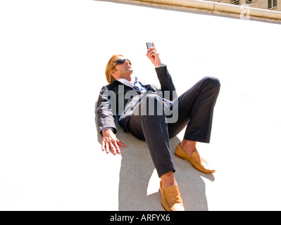 Ein junger kaukasischen Geschäftsmann mit Blackberry auf eine konkrete Steigung in der Sonne liegen Stockfoto