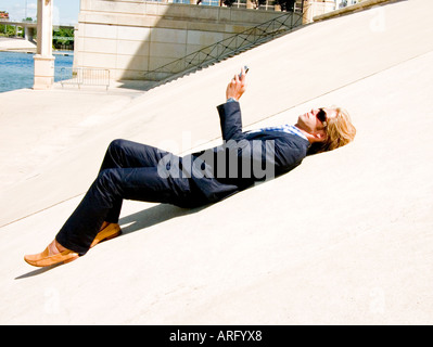 Ein junger kaukasischen Geschäftsmann mit Blackberry auf eine konkrete Steigung in der Sonne liegen Stockfoto