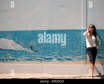 einem niedrigen Winkel Schuss junge Frau gelehnt ein Wandbild des Surfers auf Welle sprechen auf ihrem Handy Stockfoto