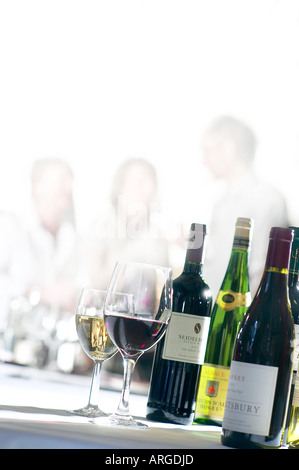 ROT- UND WEIßWEIN AUF EINEM TISCH BEI EINER WEINPROBE MIT MENSCHEN IM HINTERGRUND Stockfoto