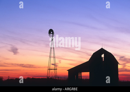 Ein schöner Sonnenuntergang mit einer Windmühle und Scheune Silhouette gegen den Abendhimmel im ländlichen Indiana USA Stockfoto