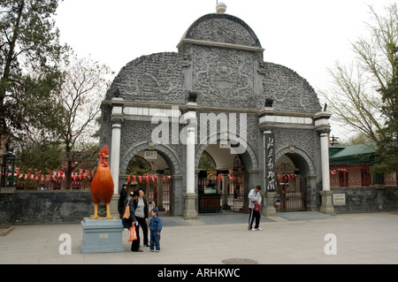 Besuchern stehen neben einer Statue von einem roten Hahn vor dem historischen Eingang in Peking Zoo Stockfoto