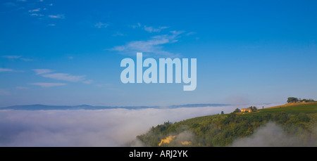 Ein Ferienhaus Villa und Farm auf einem Hügel in der Toskana sonnt sich in einem blauen Himmel und Sonne am frühen Morgen wie Nebel im Tal tief sitzt. Stockfoto