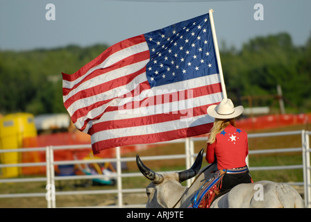 Weibliche Cowgirl reitet einen Brama Stier die Flagge in der Zeremonie vor einem rodeo Stockfoto