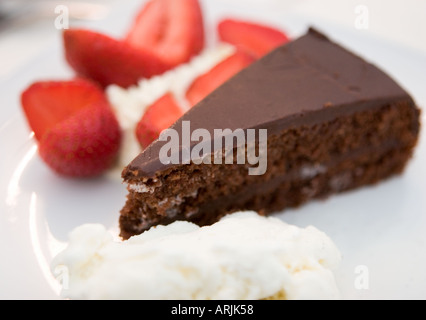 Ein Stück Schokolade Fudge Kuchen auf einem weißen Teller serviert mit Eis und Erdbeeren und frischer Sahne Stockfoto