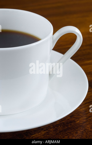 Eine Porzellantasse frisch gebraut und goss Kaffee auf eine weiße Untertasse Stand auf einem dunklen Holztisch Stockfoto