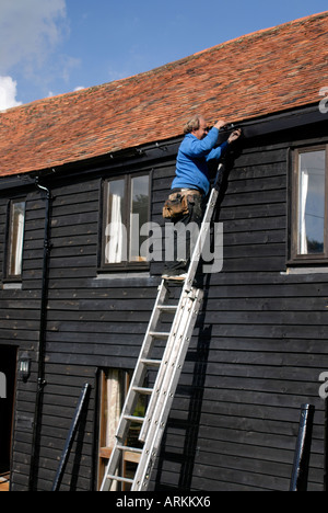 Neue schwarze Gusseisen Dachrinnen und Fallrohr installiert wird, durch einen Fachmann auf einer schwarzen weatherboarded Scheune Stockfoto