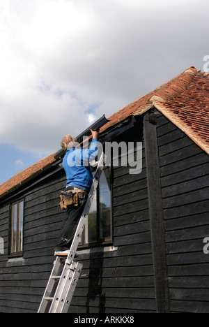 Neue schwarze Gusseisen Dachrinnen und Fallrohr installiert wird, durch einen Fachmann auf einer schwarzen weatherboarded Scheune Stockfoto