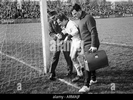 Fußball, Regionalliga West 1964/1965, Sportfreunde Hamborn 07 gegen Borussia Mönchengladbach 1:3, Stadion Im Holtkamp in Duisburg verletzt-Football-Spieler, Heinz Willi Rassmanns wird geführt vom Spielfeld durch eine Ambulanceman und Masseur Charly Lager (rechts) Stockfoto