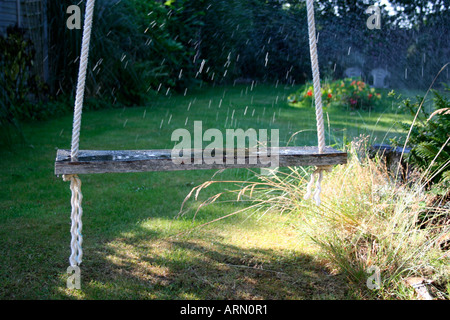 Rustikale hausgemachte Schaukel in einem englischen Garten. Dorset. VEREINIGTES KÖNIGREICH. Sprinkler, die Bewässerung der Pflanzen.  Sommer. Stockfoto