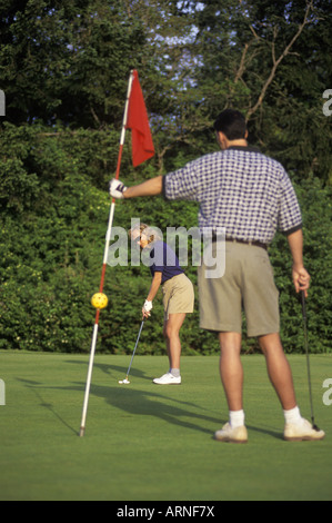 Golfspielerin Putts auf Golf grün wie männliche Golfer hilft durch Anheben der Fahne aus dem Loch, Britisch-Kolumbien, Kanada. Stockfoto