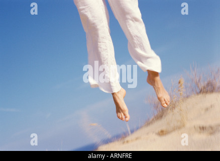 weibliche Beine springen in der Luft von Sanddüne Stockfoto