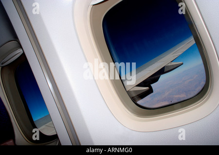 Blick durch das Fenster des Flugzeugs von der Tragfläche vor einem tiefblauen Himmel Stockfoto