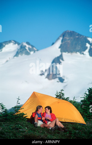junges Paar Camps in Wiese mit Bergkulisse in alpinen Whistler, Whistler, Britisch-Kolumbien, Kanada. Stockfoto