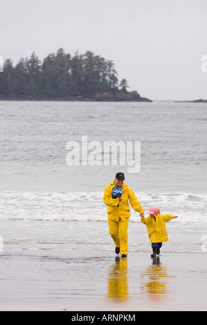 Mutter und Tochter in gelb Regenbekleidung laufen Beach, MacKenzie Beach am Tofino, Vancouver Island, British Columbia, Kanada. Stockfoto