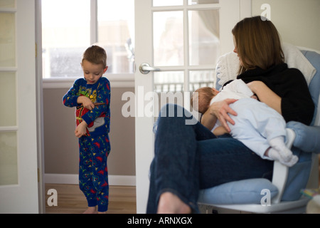 Mutter stillen Kind zu Hause während der vier Jahre alten Bruder steht in der Nähe Stockfoto