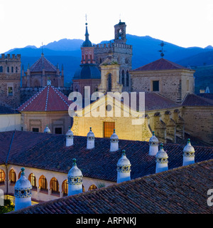 Guadalupe, Extremadura, Spanien. Die Real Monasterio de Santa María de Guadalupe in der Abenddämmerung, Dach des Parador im Vordergrund. Stockfoto