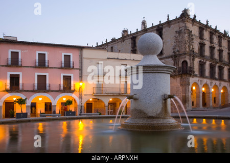 Trujillo, Extremadura, Spanien. Brunnen auf dem beleuchteten Plaza Mayor in der Abenddämmerung, im 16. Jahrhundert Palacio De La Conquista darüber hinaus. Stockfoto