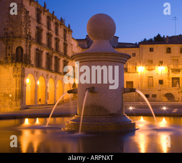 Trujillo, Extremadura, Spanien. Brunnen auf dem beleuchteten Plaza Mayor in der Abenddämmerung, im 16. Jahrhundert Palacio De La Conquista darüber hinaus. Stockfoto