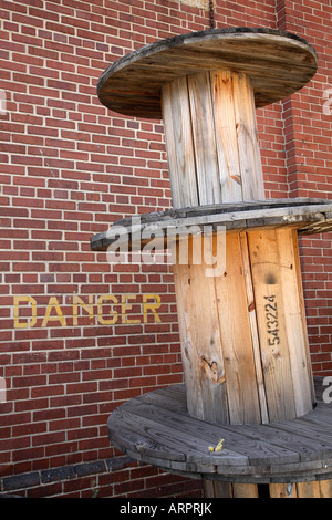 Große leere hölzerne Rollen verwendet, um Loch Kabel neben Ziegelwand mit dem Wort Gefahr aufgedruckt. Stockfoto