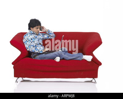 VDA200166 südasiatischen indischer Mann auf Sofa am Laptop arbeiten und sprechen auf mobile tragen Jeans und Hemd, Herr 701 Stockfoto