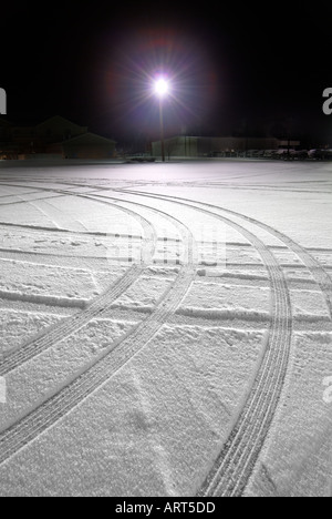 Reifenspuren im Schnee in der Nacht, einsame Licht auf Parkplatz Stockfoto
