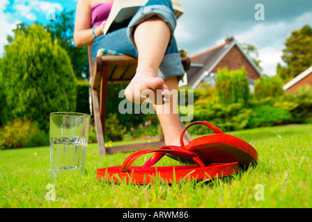 Frau sitzt auf dem Liegestuhl im Garten mit Schuhen auf dem Rasen Stockfoto