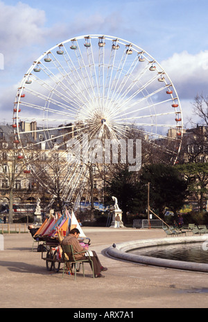 Paris Teich im Jardin des Tuileries mit einem Mann, der neben Miet- und Spielsegelbooten sitzt, und einem großen, sich drehenden Riesenrad dahinter in Frankreich, Europa, EU Stockfoto