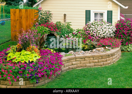 MINNESOTA GARTEN MIT BLUMENERDE HAUS, WASSERFALL UND TEICH. WAVE PETUNIEN, SWEET POTATO VINE, OLEANDER, CANNA, COLEUS UND HYAZINTHE. Stockfoto