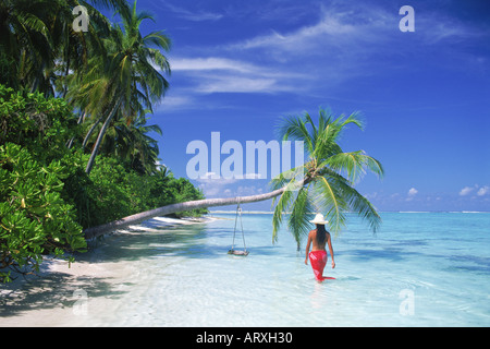 Frau trägt rote Sarong und weißen Hut Strand entlang mit überhängenden Palme in Malediven Stockfoto