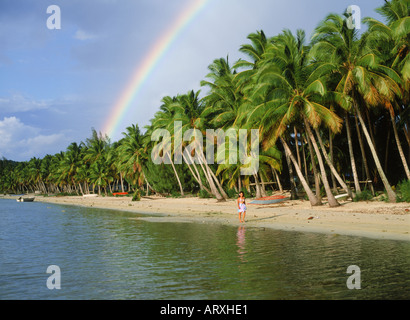 Polynesische Frau zu Fuß unter Regenbogen und Palmen auf Aitutaki Lagune, Cook-Inseln Stockfoto