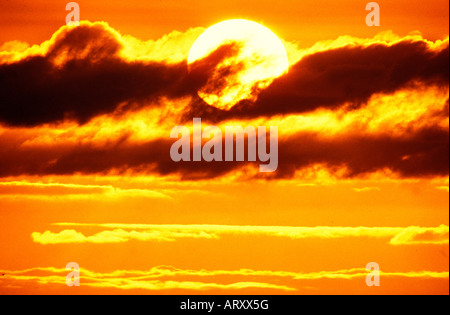 Sonnenuntergang hinter dunklen Wolken am Himmel leuchtet orange Stockfoto