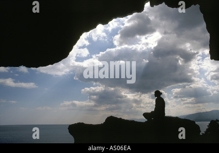 Eine Person in der Silhouette sitzt in einer Höhle mit Wolken und Meer Stockfoto