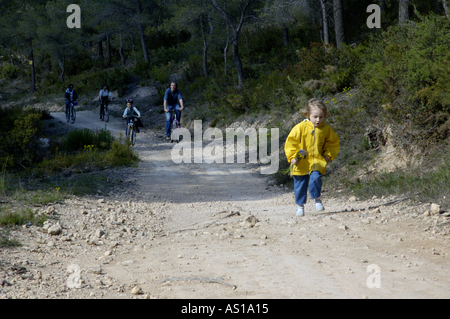 Mädchen vor ihrer Familie auf einer unbefestigten Straße laufen, während sie hinter Vitrolles, Provence, Frankreich-Zyklus. Stockfoto