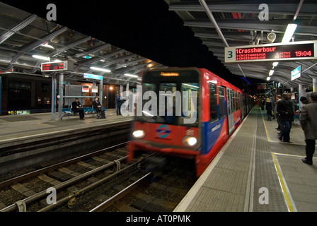 Horizontalen Weitwinkel der Docklands Light Railway Zug Ankunft an Poplar Station mit Menschen warten auf die Plattform in der Nacht Stockfoto