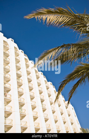 Vertikale Weitwinkel von der Vorderansicht eines weißen Hotels und einer Palme gegen ein strahlend blauer Himmel Stockfoto