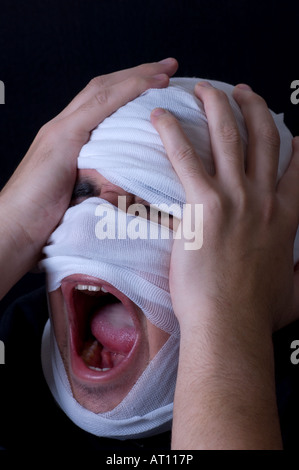 Verpackte Mann im Verband in extremen Schmerzen schreiend die Hände auf den Kopf Stockfoto