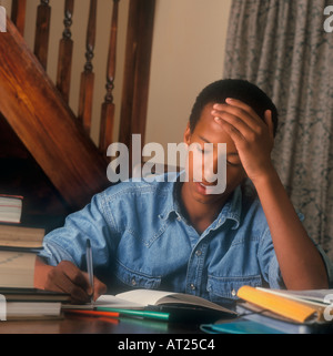 Hausaufgabenkunde 14-16 Jahre Junge Heimschularbeit Bücher Teenage Black African Caribbean Schoolboy studiert intensiv mit seiner Prüfungsaufgabe Stockfoto