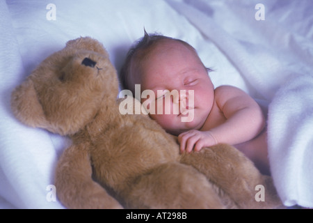 Baby schläft mit Teddybär Kumpel auf einem Bett aus weißen Laken wie eine Wolke Stockfoto