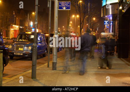 perfekte Menschen und Touristen zu Fuß vorbei an Pubs und Clubs auf Bradbury stellen Belfast neben Taxi Taxistand Stockfoto