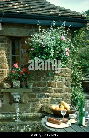 Tisch vor der Hütte Wand mit hängenden Korb über Löwen Kopf Wasser Brunnen und Stein Waschbecken Stockfoto