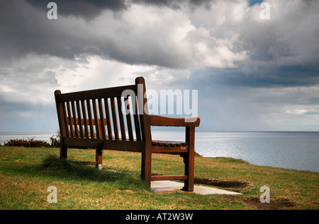 Eine leere nasse Holzbank blickt auf das Meer und gefüllte Wolken regnen Stockfoto