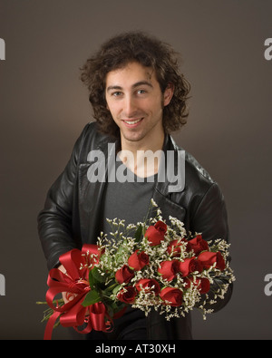 20 etwas lächelnder Mann Mann in schwarzer Lederjacke halten ein Dutzend rote Rosen Stockfoto