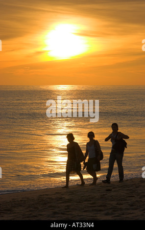 Drei Erwachsene, ein Spaziergang am Strand entlang zum Sonnenuntergang Stockfoto