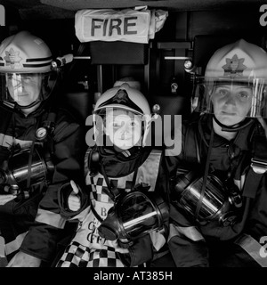 Ein Junge sitzt in einem Feuerwehrauto mit zwei Feuerwehrmänner Stockfoto