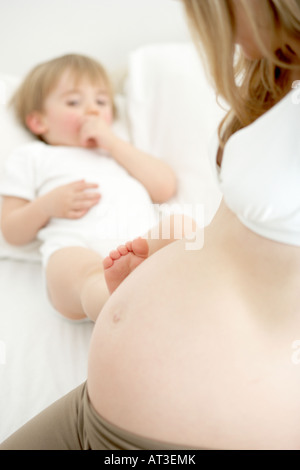 Ein kleiner Junge, der seinen Fuß auf seine Mutter schwanger Bauch ruht Stockfoto