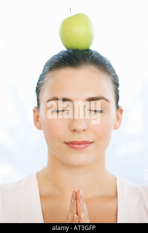 Junge Frau mit einem Apfel auf dem Kopf, die Augen geschlossen, Hände im Gebet Stockfoto